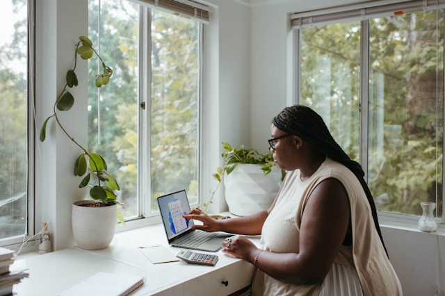 Remote worker using a laptop in a home office setting, ensuring cybersecurity while working from home, surrounded by natural light and plants.